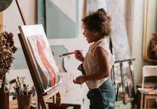 Young girl smiling at a canvas she is painting on